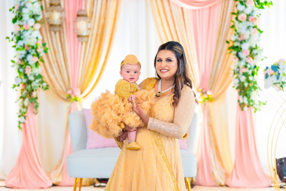 Mother and baby in matching yellow outfits pose against peach and gold backdrop with greenery.