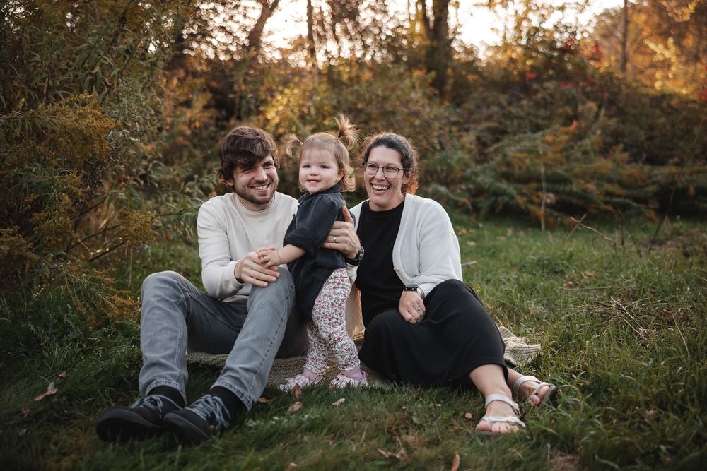 A family sits together on grass during golden hour in an outdoor autumn setting.