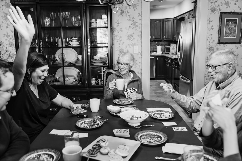 A black and white photograph of a family gathered around a dining table for a meal, with hands raised in laughter.