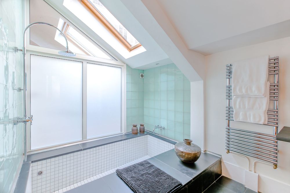 Skylit bathroom with mint green tiles, large soaking tub, frosted windows, and heated towel rail.