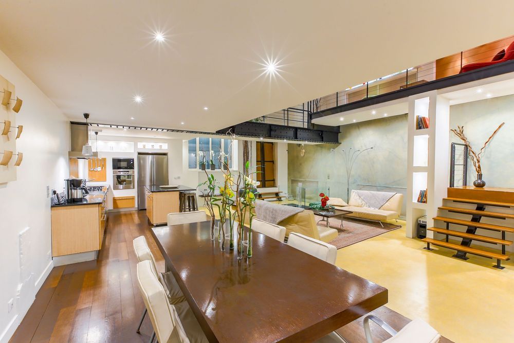 Stylish open-plan dining and living space with dark wood table, mezzanine level, and modern kitchen.
