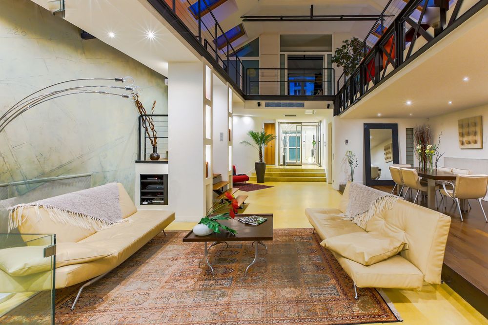 Spacious living room with cream sofas, Persian rug, glass coffee table, and mezzanine level above.