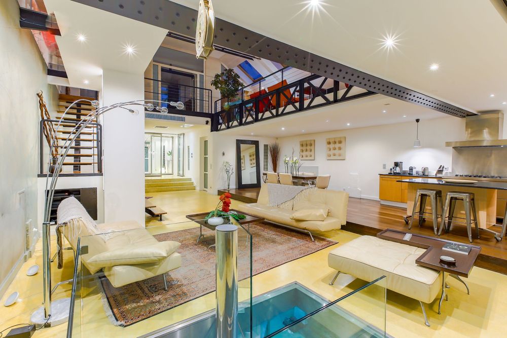 Luxurious open-plan loft living space with mezzanine level, spiral staircase, modern furniture, and sleek kitchen area.