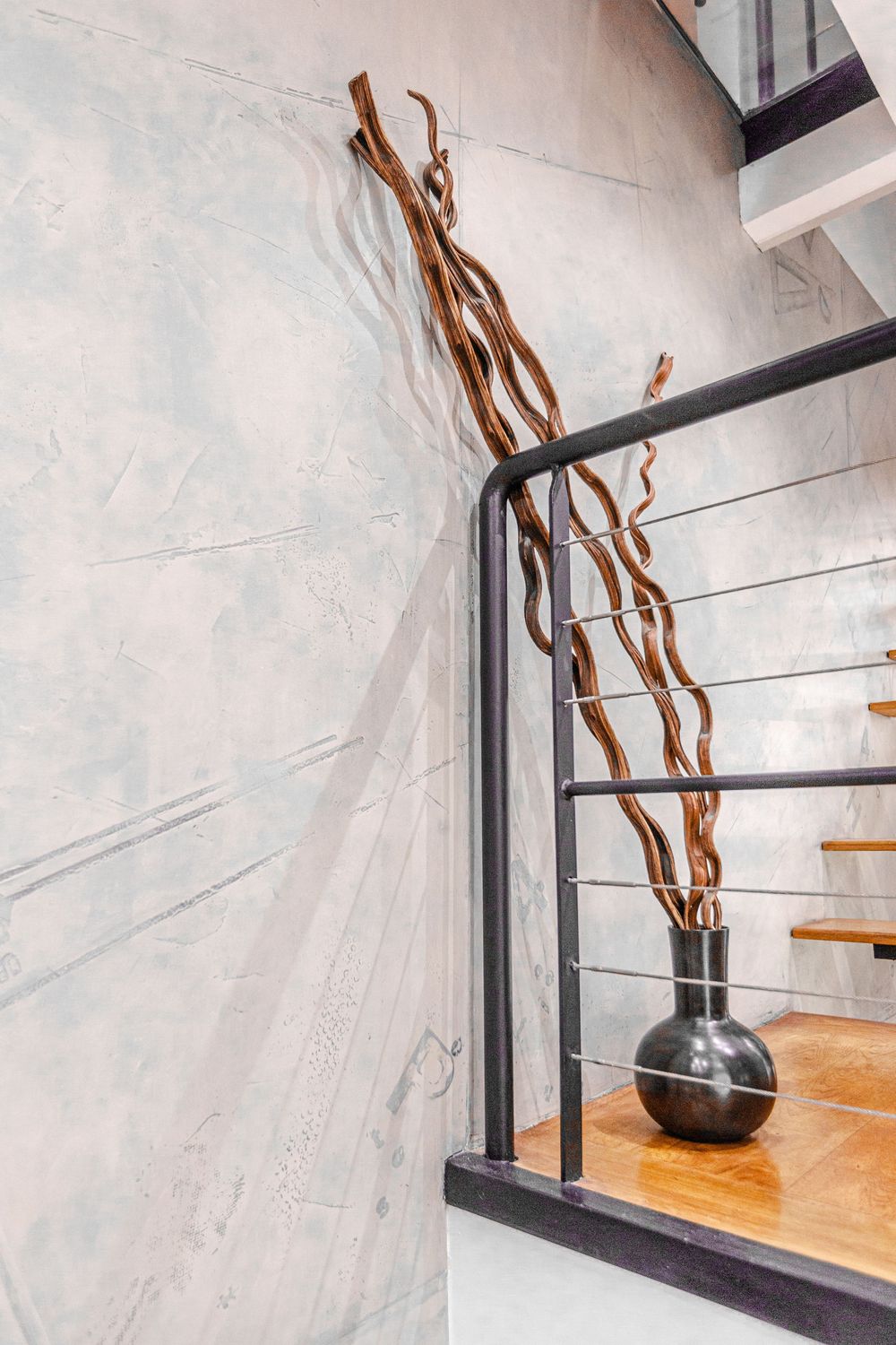 Modern staircase with black metal railing, decorative twisted branch vase, and textured marble wall in contemporary home.