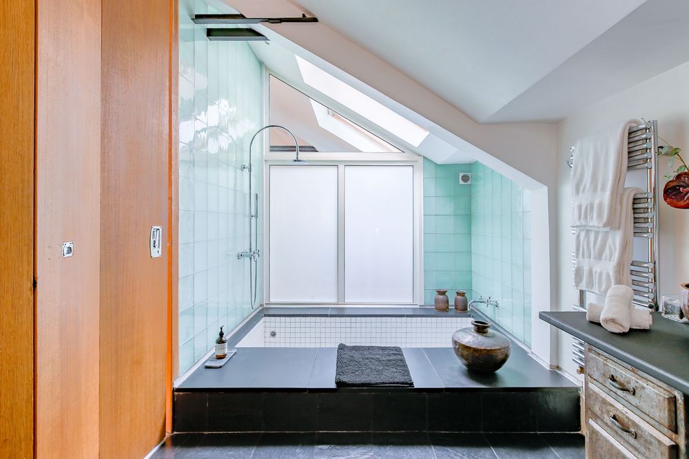 Angled ceiling bathroom featuring mint green tiled shower area, skylight, and modern heated towel rack.