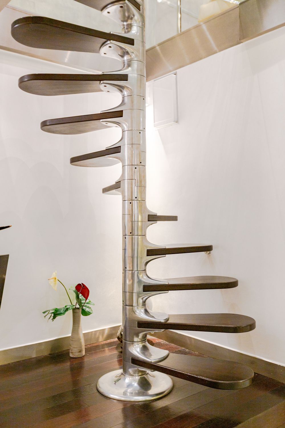 Elegant chrome spiral staircase with dark wood treads, polished metal central column, and minimalist white interior design.