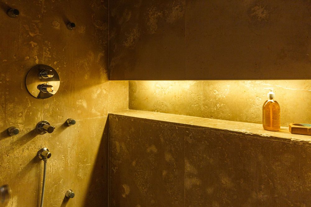Luxurious golden-lit shower niche with textured walls, multiple shower jets, and amber-lit built-in shelf with toiletries.