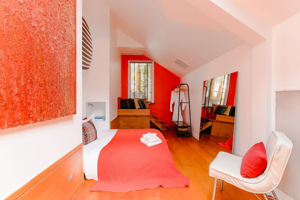 Vibrant bedroom with red accent wall, red bedspread, large artwork, and natural wood flooring.
