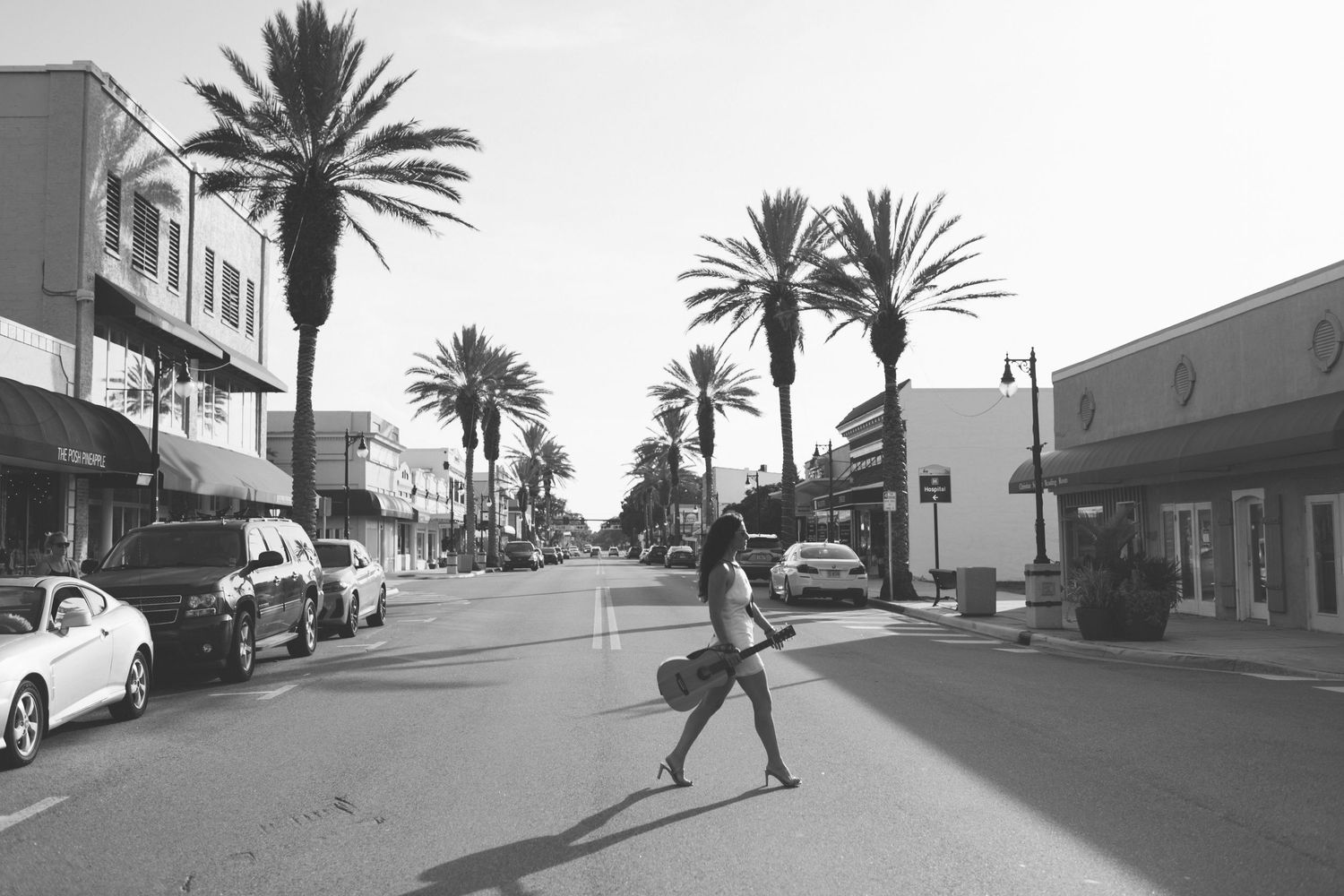Black and white street scene with palm trees and a person running through a town.