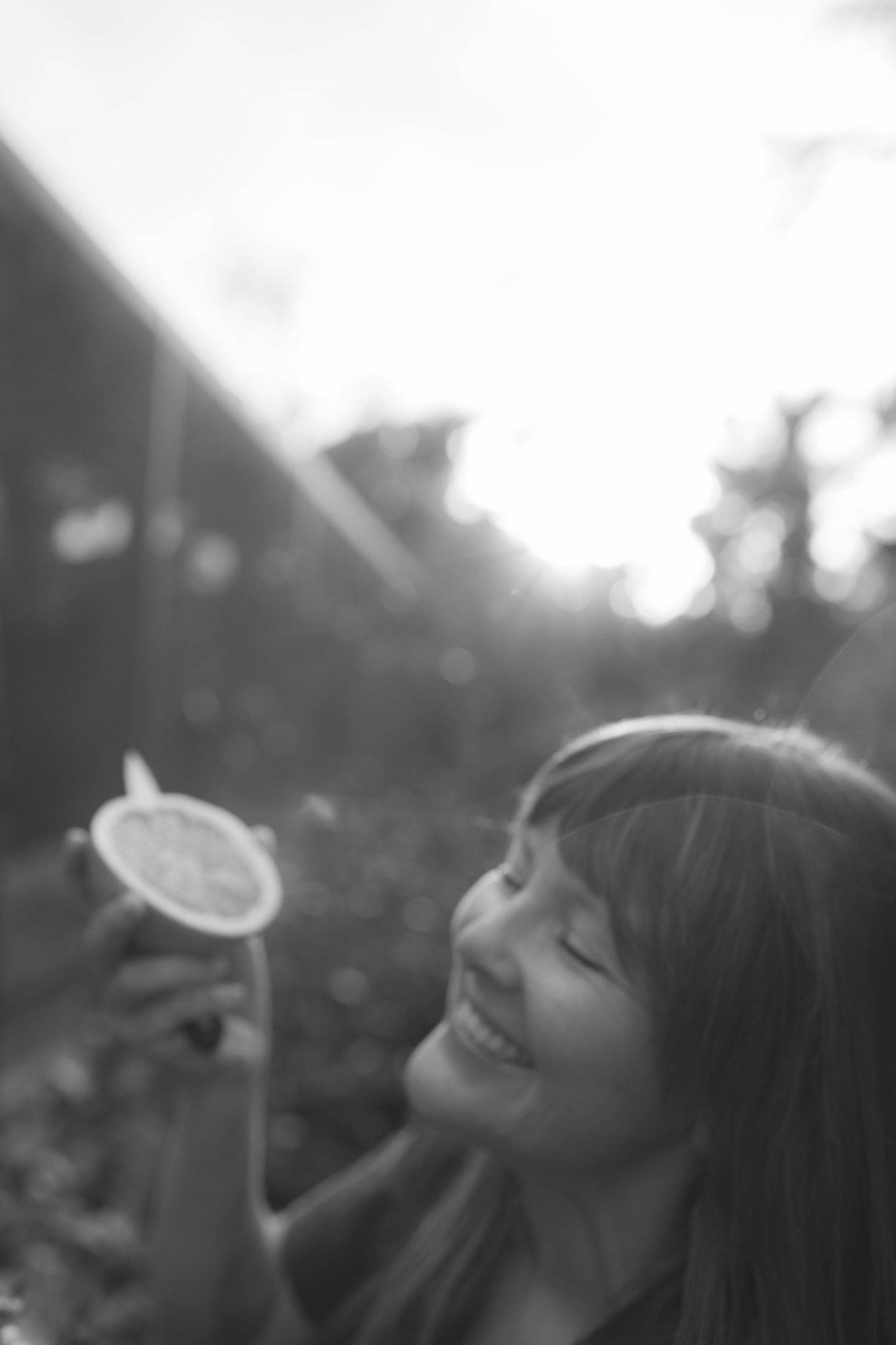 A dreamy black and white portrait of someone holding a dandelion flower in sunlit garden.