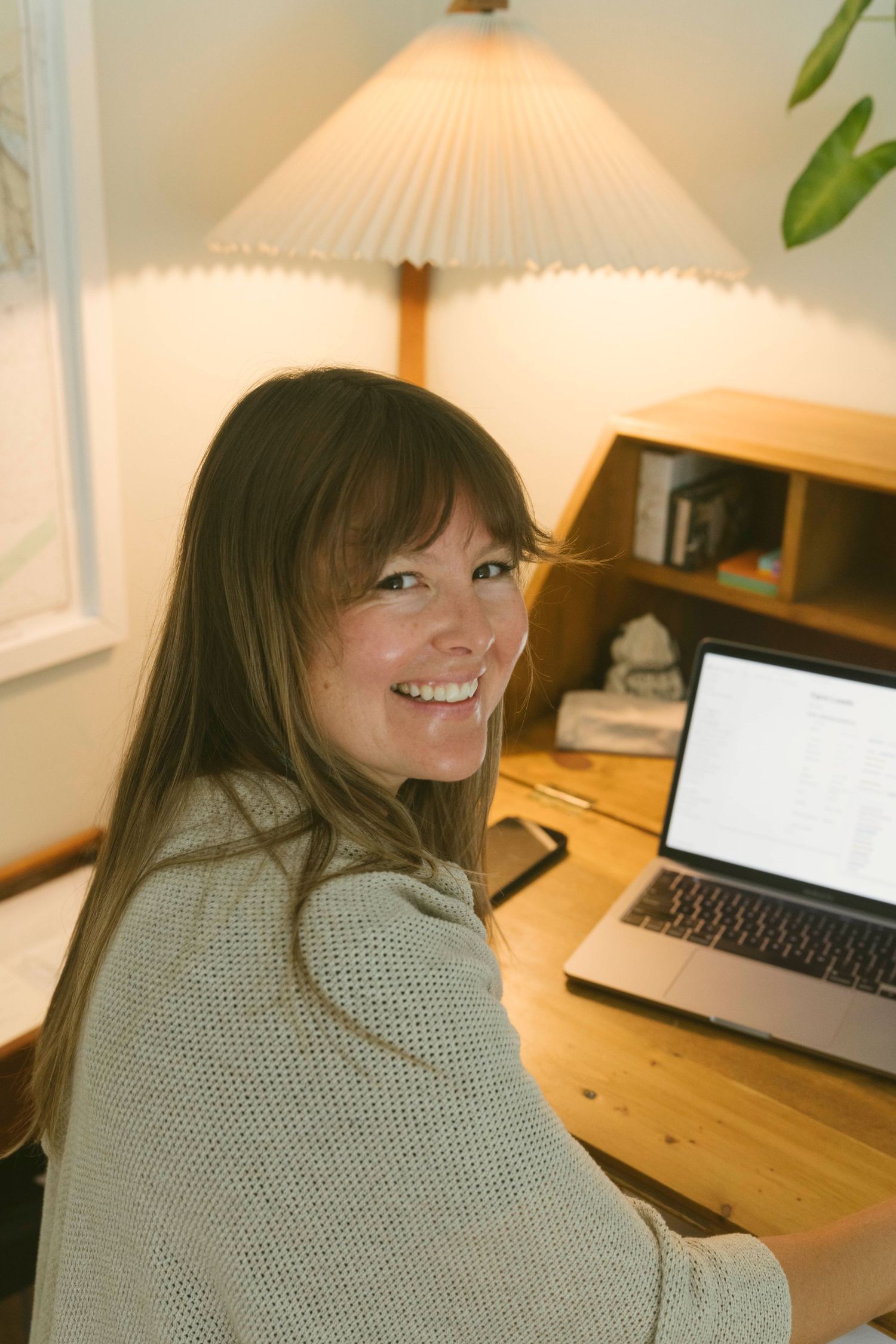 Person working at wooden desk with laptop and desk lamp in cozy home office setting.