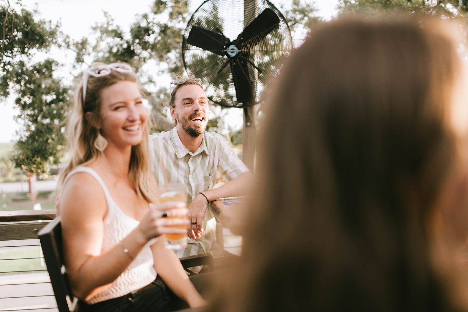 Friends sharing drinks and conversation at an outdoor patio table.
