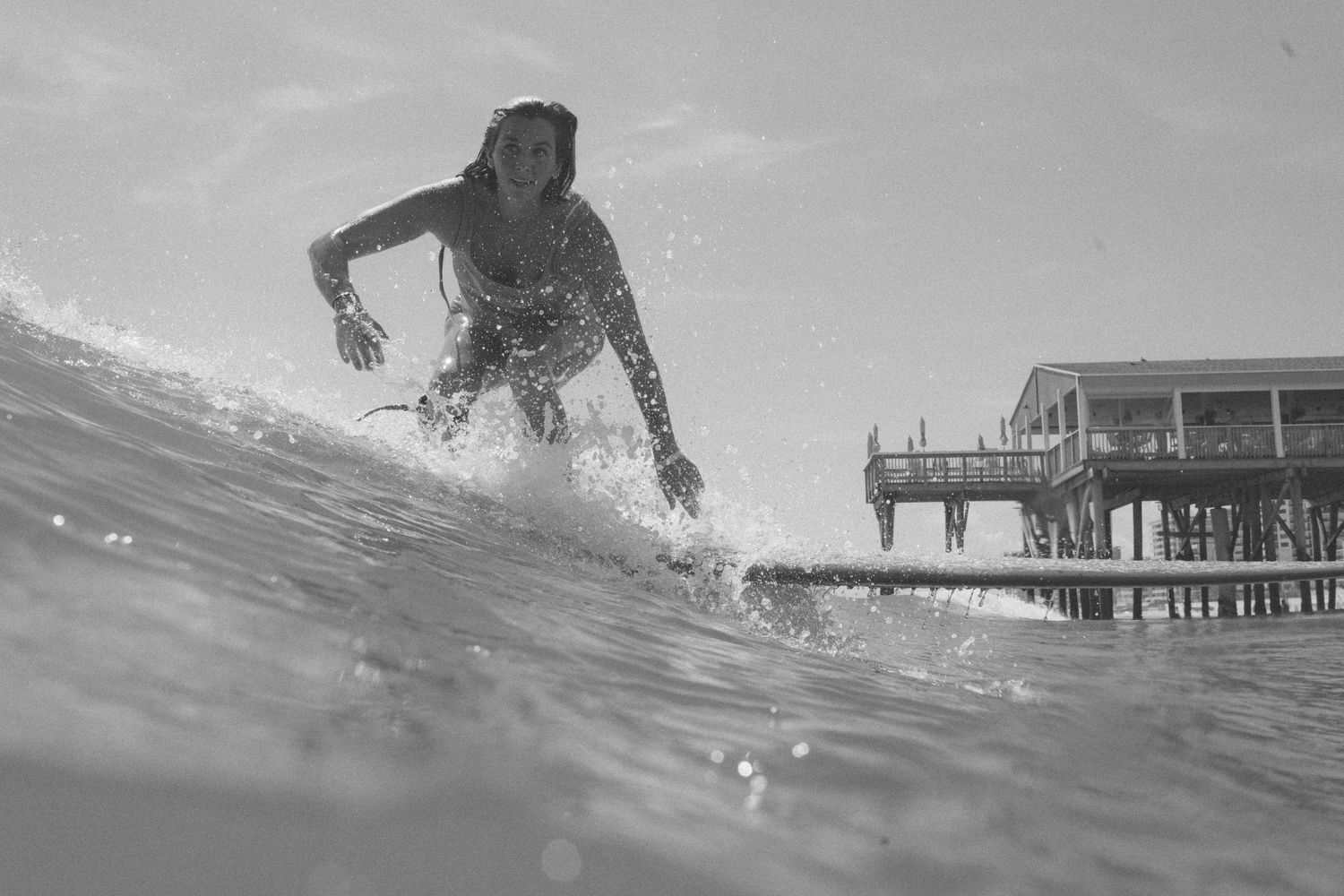 Silhouette of a surfer riding a wave near a pier in black and white photography.