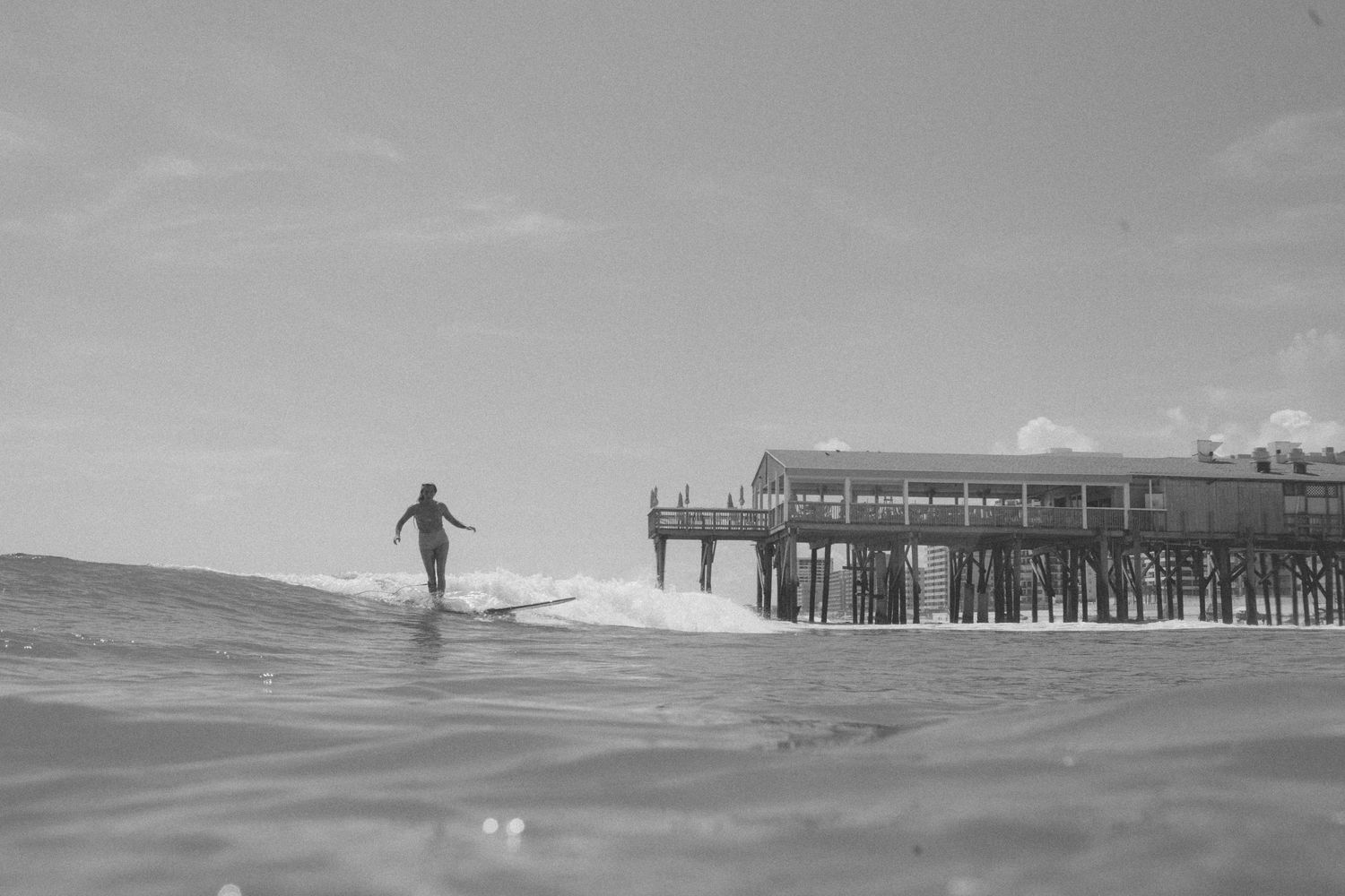 A lone surfer riding waves with a wooden pier in the background.