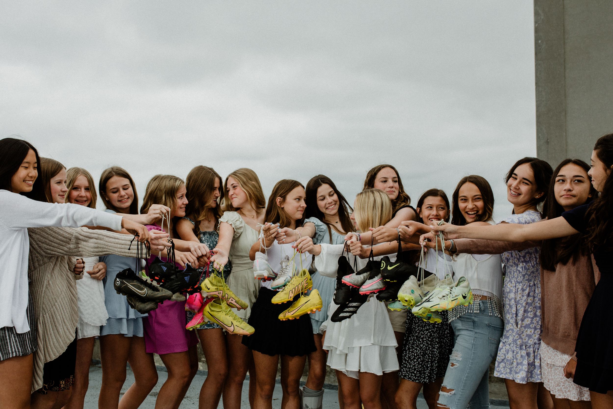 Group holding up bouquets in synchronized pose against cloudy sky.