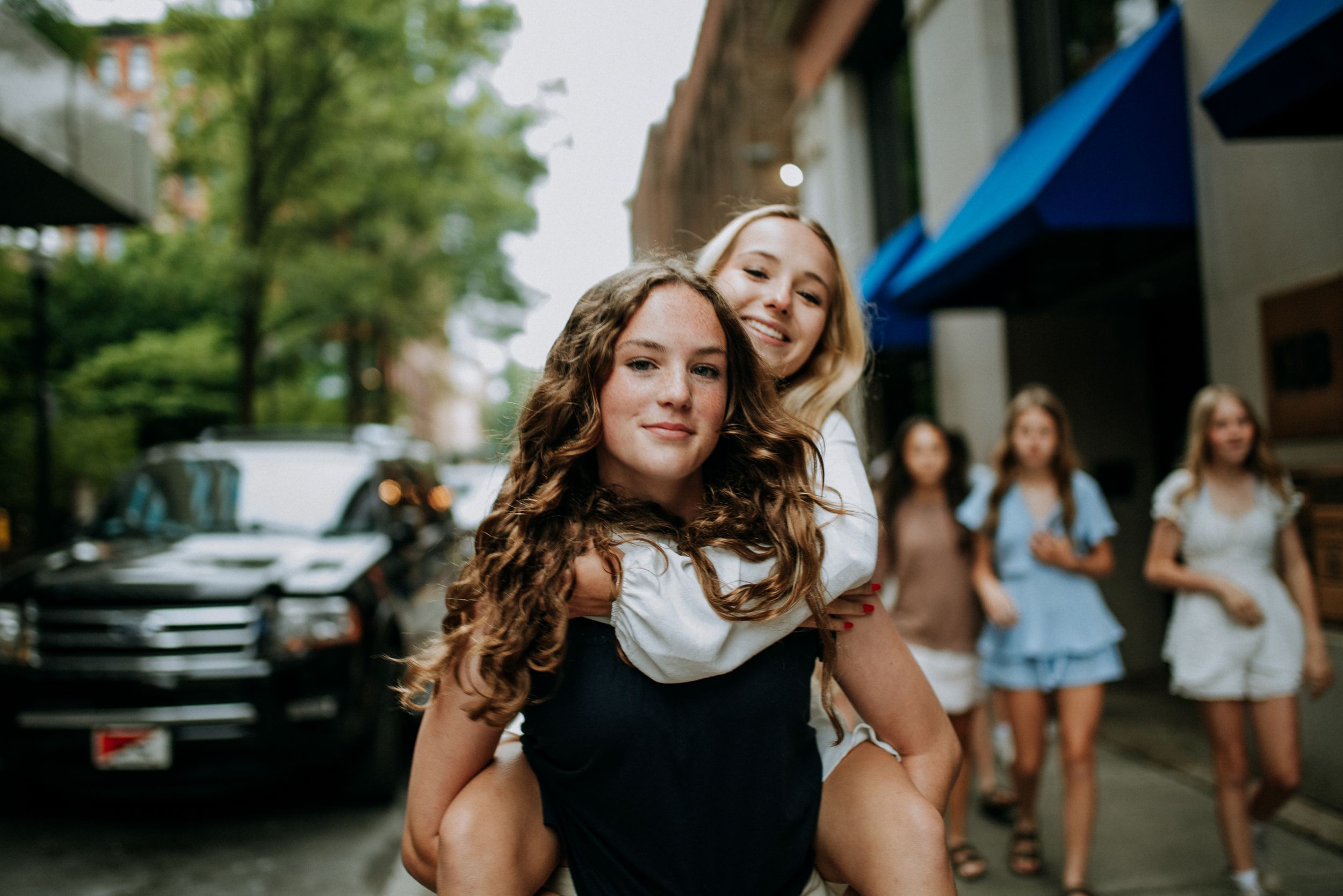 Two friends having fun together on a city street with other people visible in the background.
