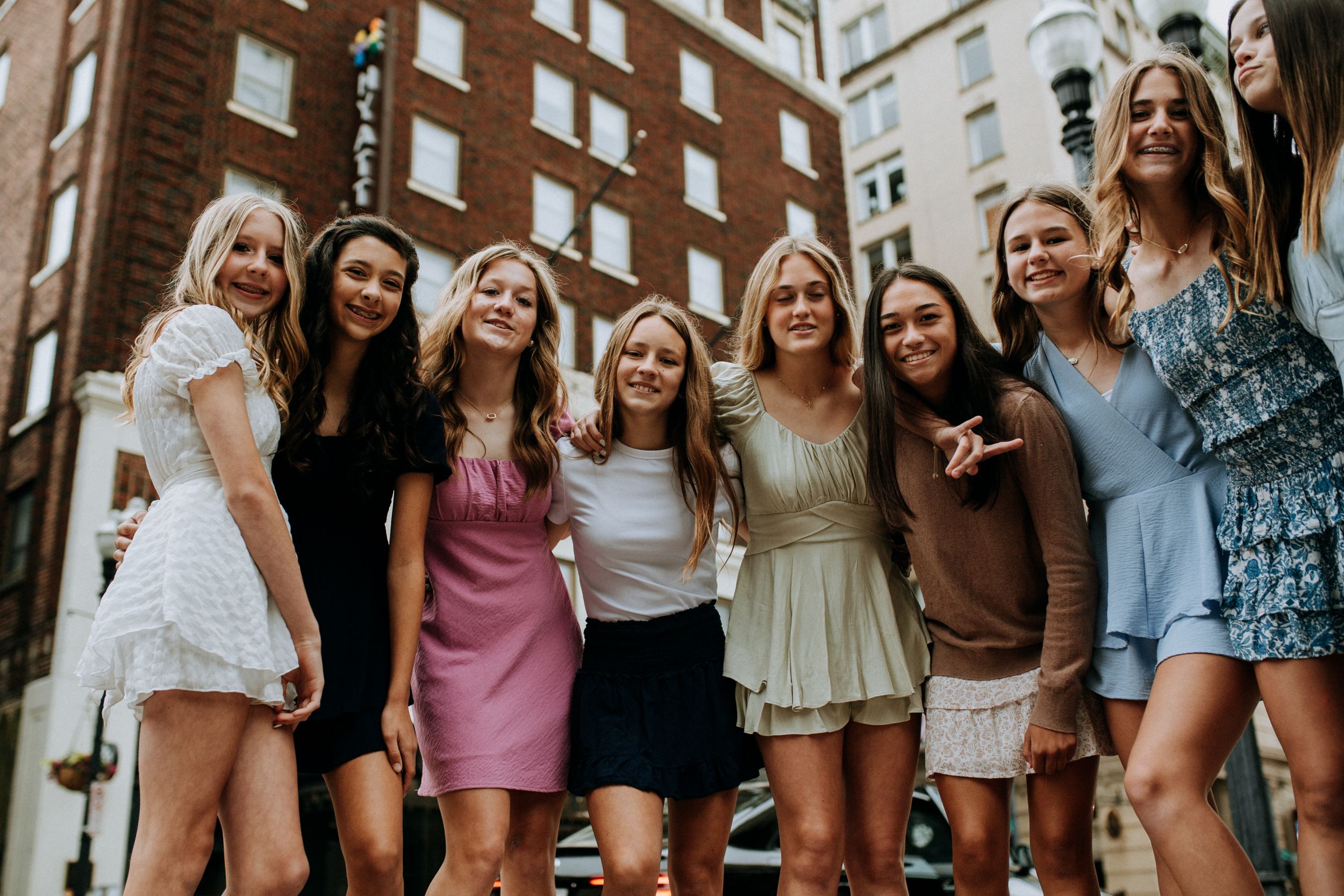 Friends gathered together smiling and posing against a brick building backdrop.