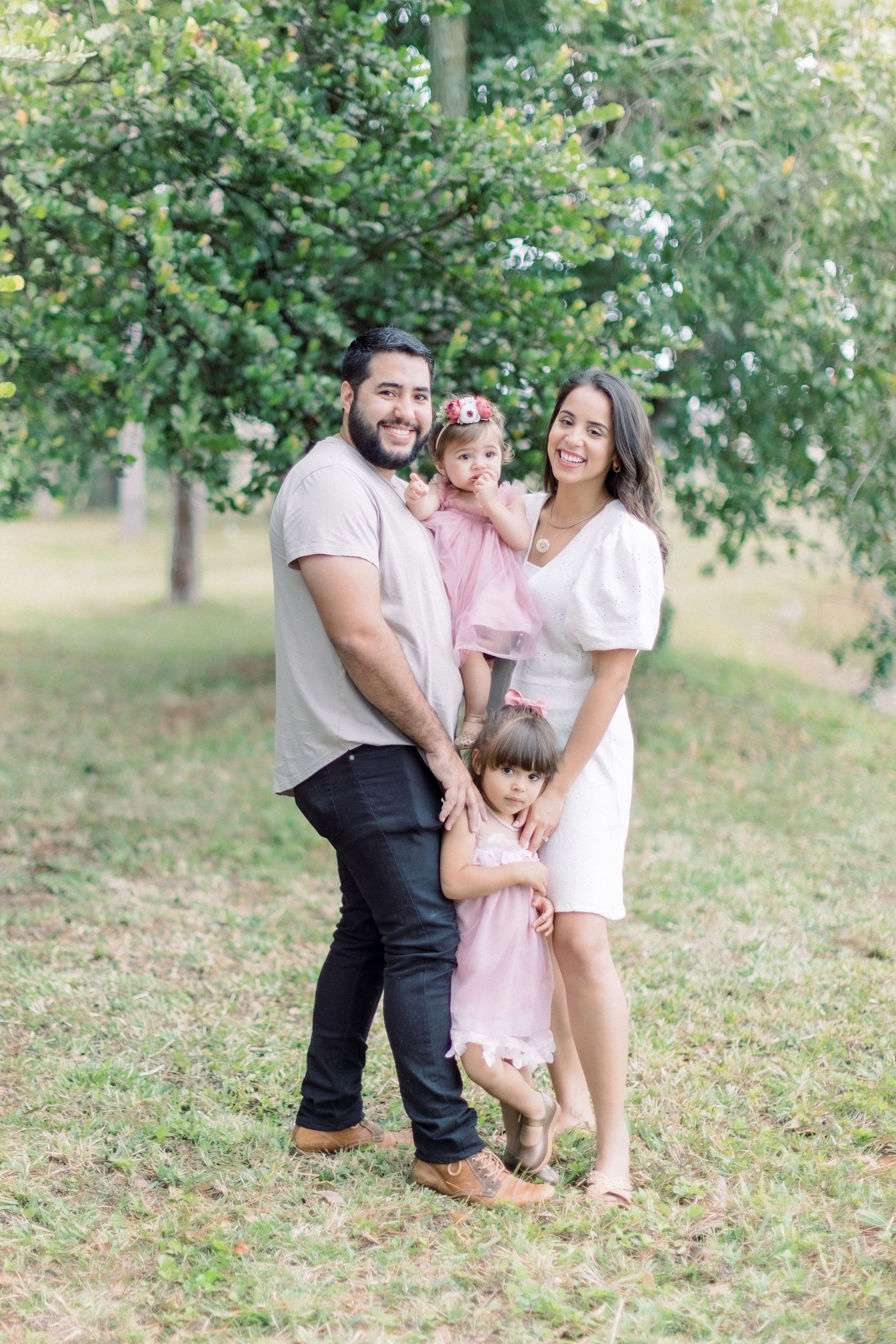 A family poses together outdoors in a park setting surrounded by greenery.