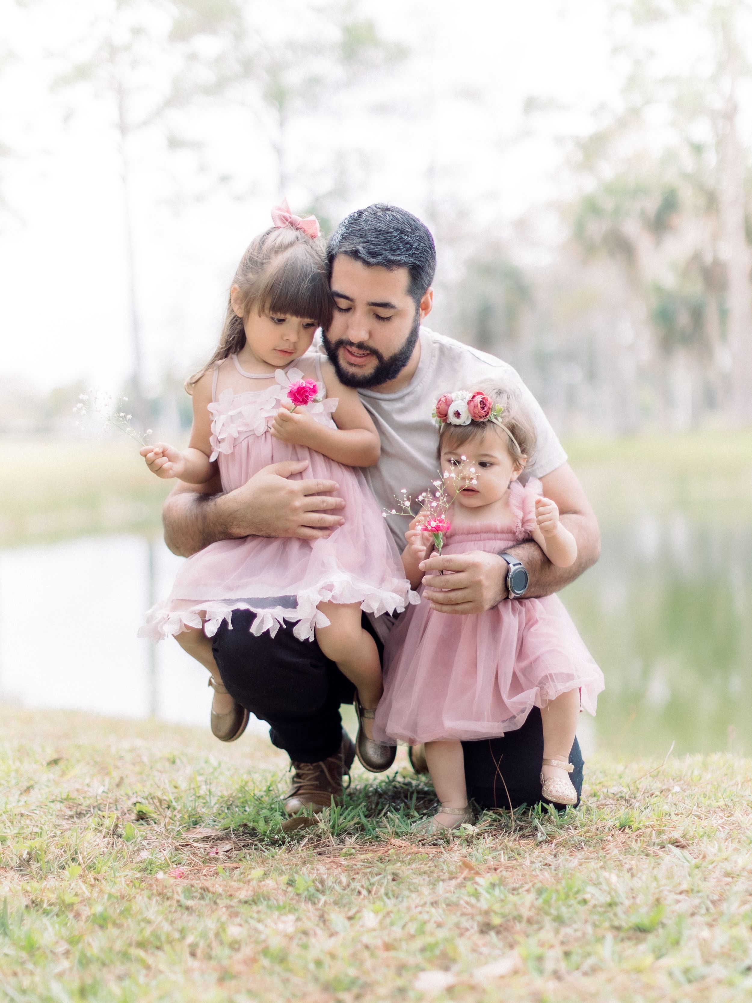 A sweet family moment captured in a park with pink dresses and flowers.