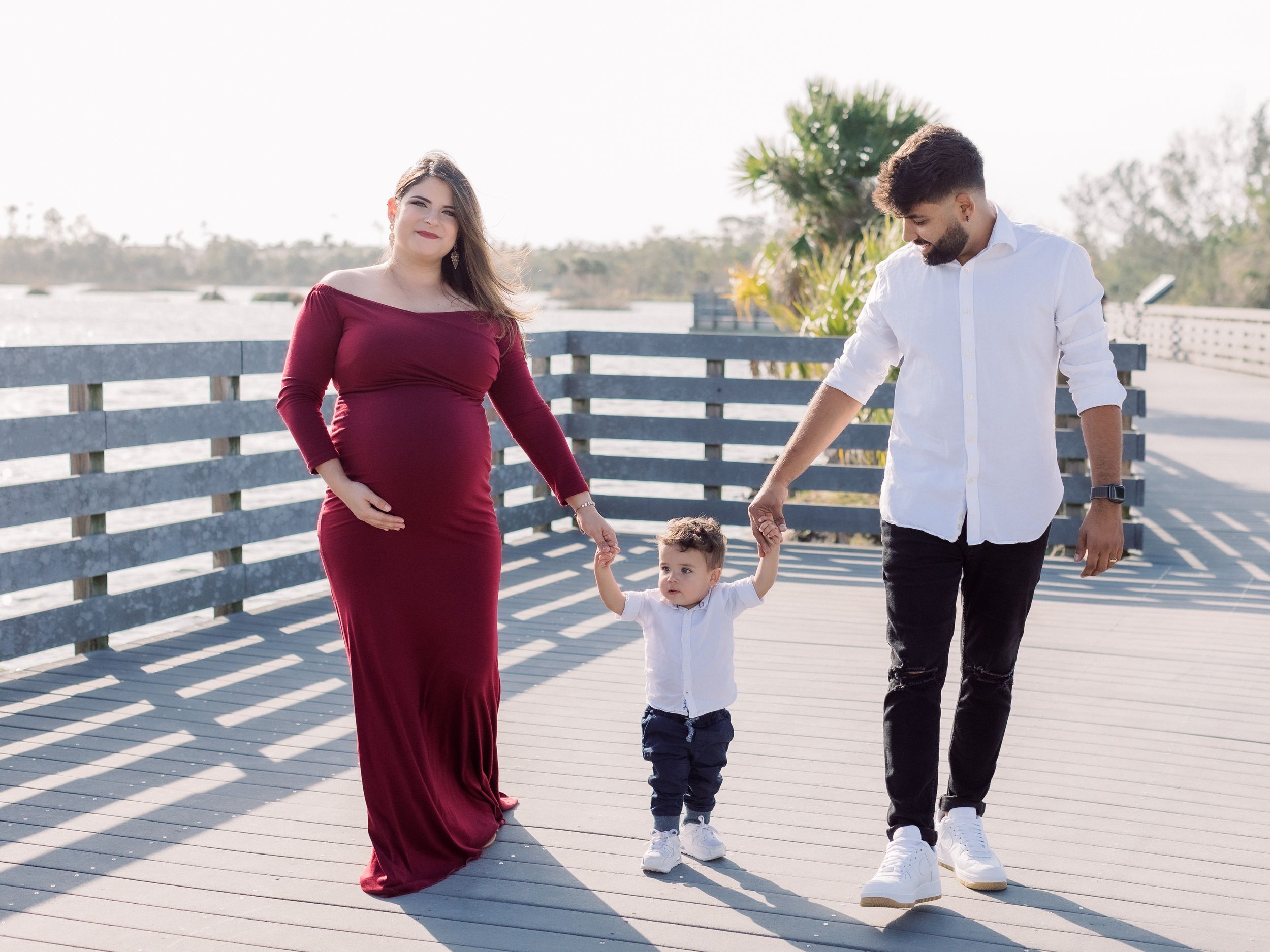A family walks together on a wooden boardwalk during a sunny day by the water.