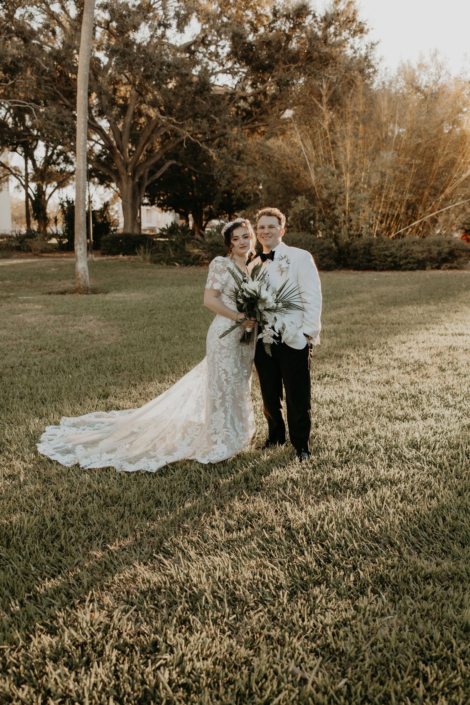 A stylish couple in wedding attire pose together against an industrial brick backdrop.