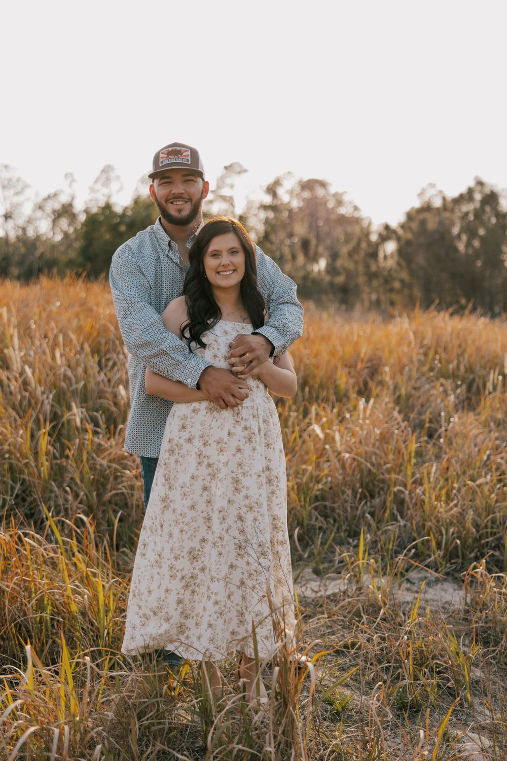 Couple shares intimate moment in field of tall grass during golden hour photoshoot.