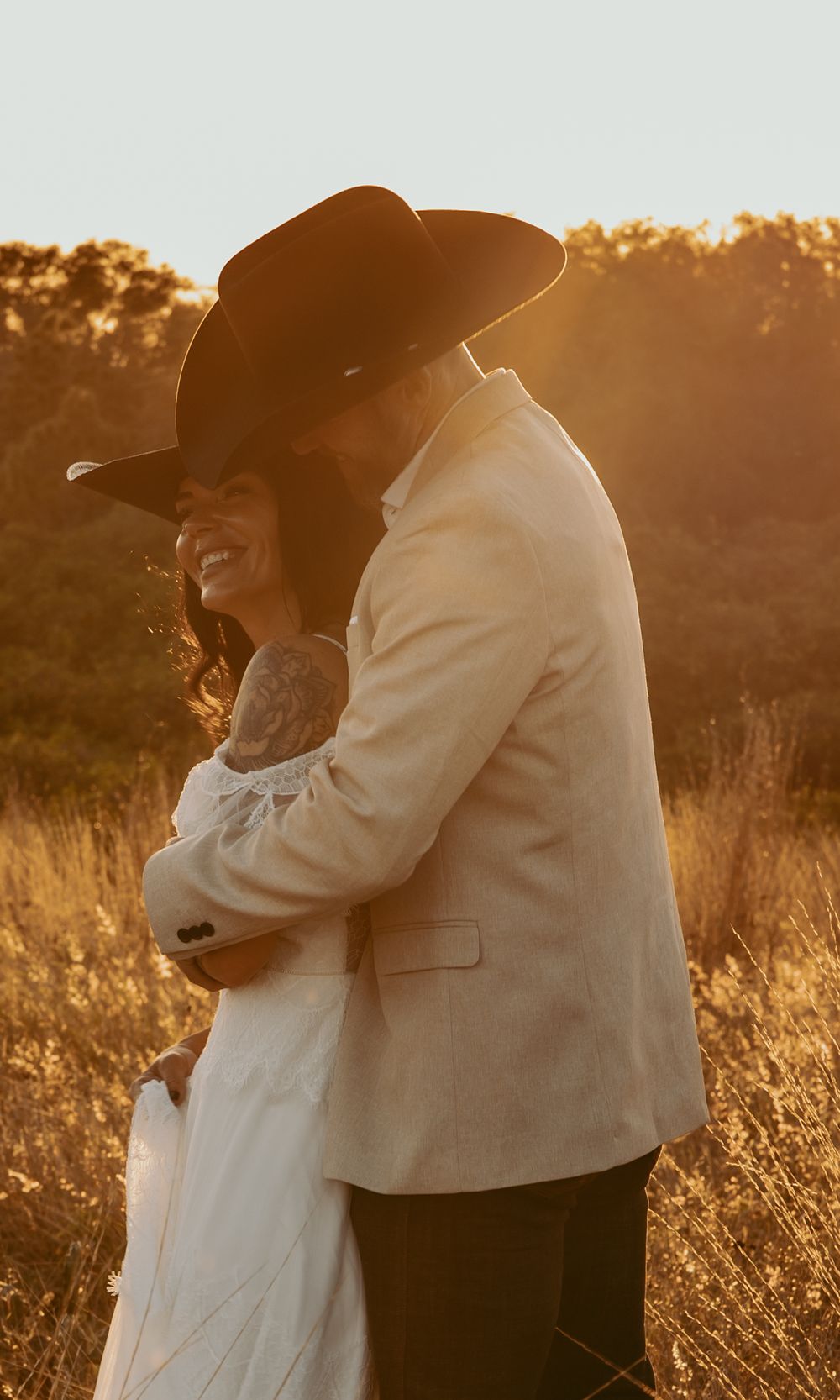 A candid moment of laughter between newlyweds in western attire during sunset.