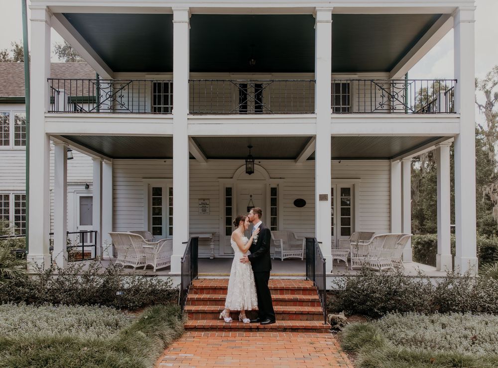 A panoramic view of a white colonial style house with columns and covered porches on a sunny day.