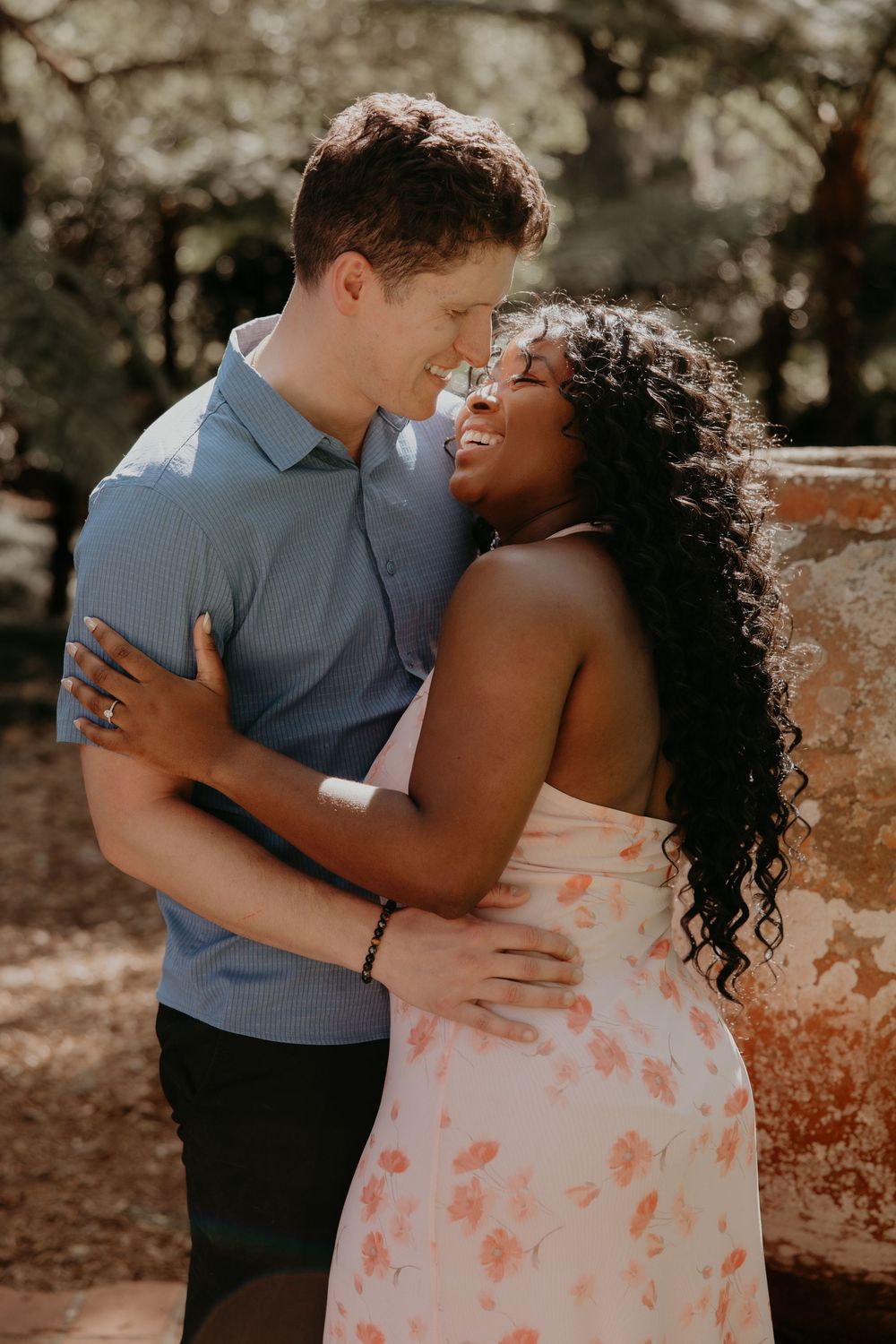 Happy interracial couple embracing and smiling at each other outdoors in a sunlit garden setting.