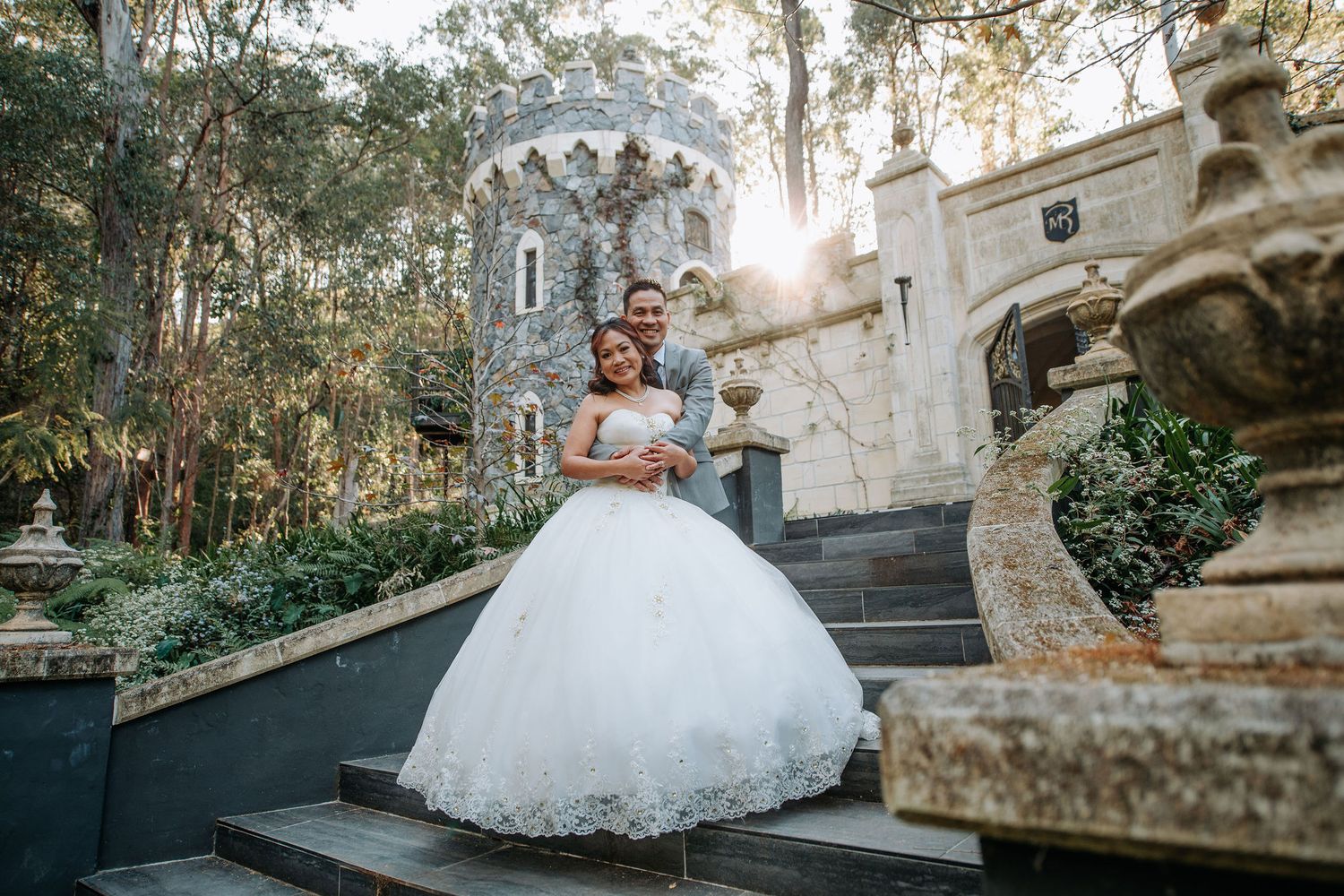 A romantic wedding photo at a castle-like venue with stone steps and towers during golden hour.