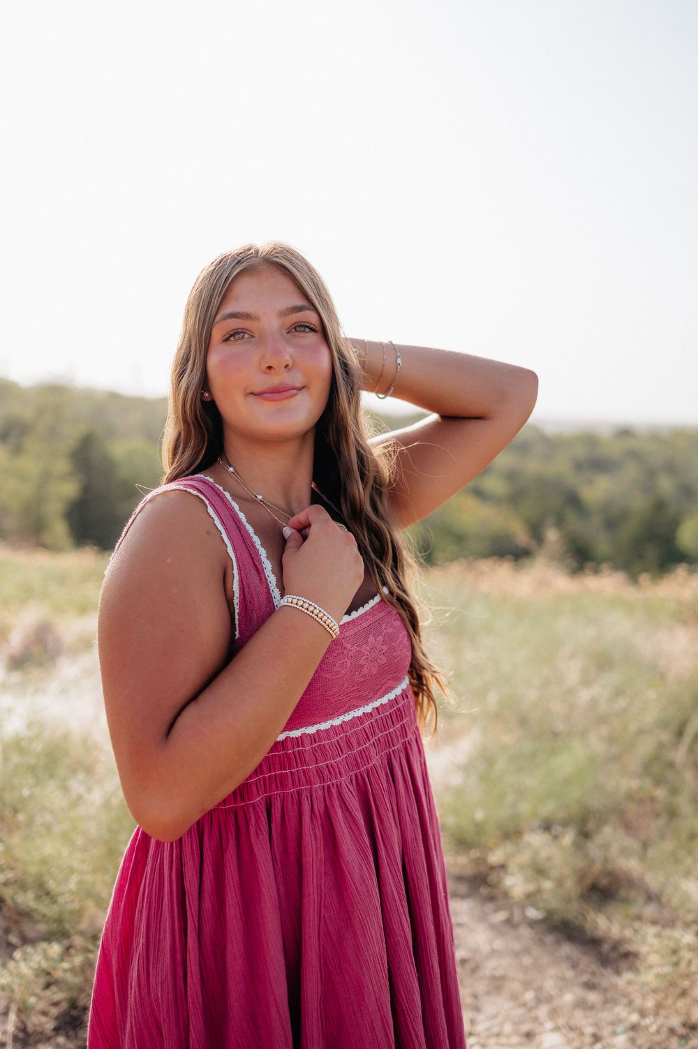 A woman in a pink summer dress poses gracefully in a sunny outdoor field setting.