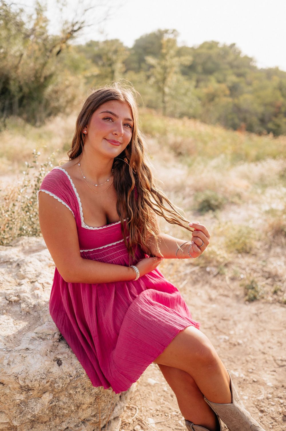 A woman in a fuchsia sundress sits on a rock along a desert hiking trail.