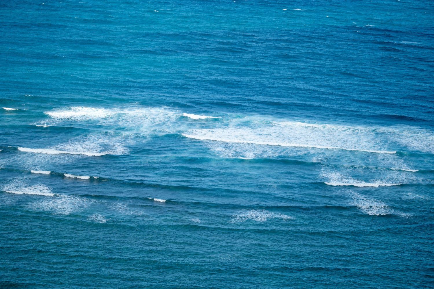 Aerial view of surfers riding blue ocean waves on a clear sunny day.
