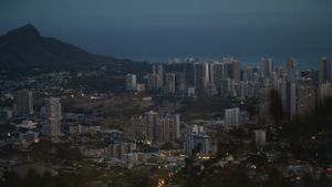 Aerial view of Honolulu cityscape at dusk with mountains in the background.