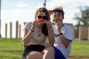 Two people enjoying watermelon outdoors on a sunny day.
