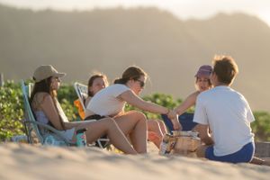 Group relaxing in beach chairs on sandy shore during golden hour with mountains in background.