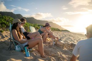 Friends gathered on beach chairs enjoying sunset with mountain backdrop.