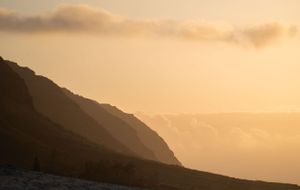 Dramatic mountain silhouettes against golden sunset sky.