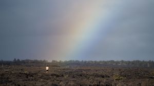 Rainbow arches over dark volcanic landscape under stormy skies.