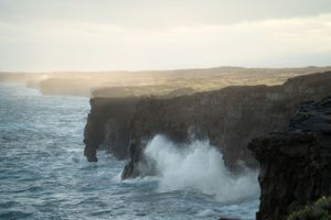 Powerful waves crash against rugged volcanic cliffs along a dramatic coastline at sunset.