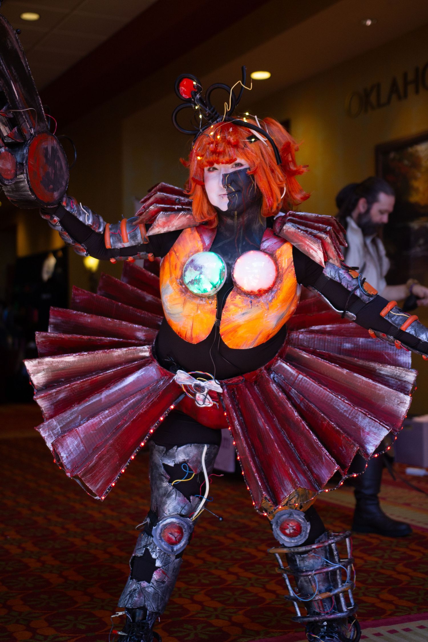A cosplayer in an elaborate steampunk-inspired costume with red pleated skirt and mechanical accessories.