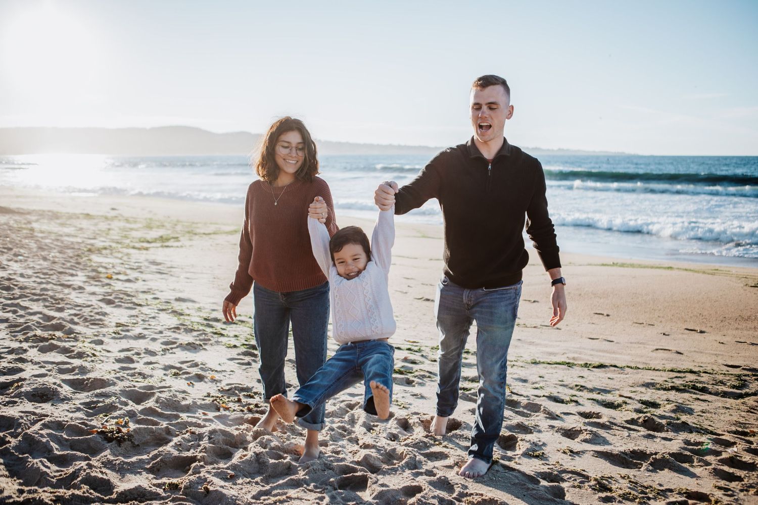 Family walking and playing together on a sunny beach with waves in the background.