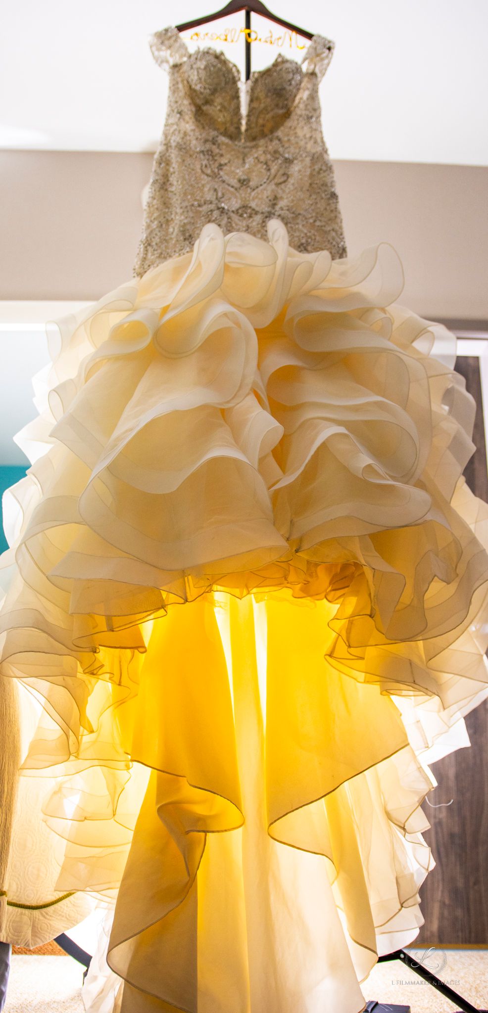 Elegant wedding dress with lace bodice and ruffled skirt hanging against backlit window.