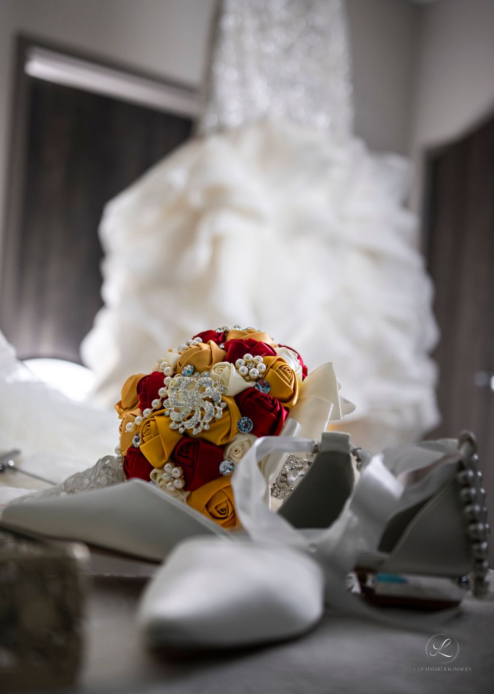 Red and gold floral wedding bouquet with white shoes and dress in soft focus background.