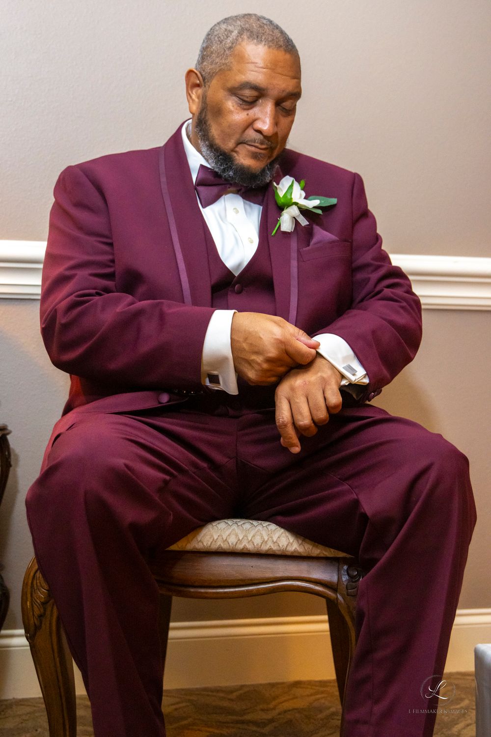 Wedding detail shot showing a person in a burgundy tuxedo sitting in an elegant chair.