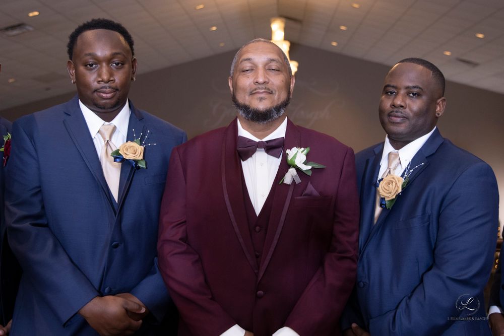Wedding party lineup wearing navy blue and burgundy suits in a formal venue.