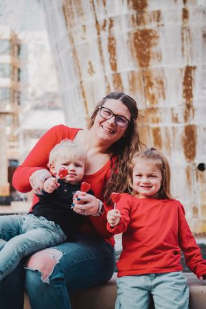 A family wearing red shirts shares joyful laughter together while sitting on a rustic bench with weathered wood background.