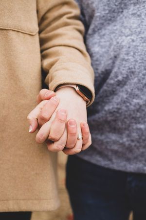 Close-up view of two hands holding each other tenderly against a gray and beige background.