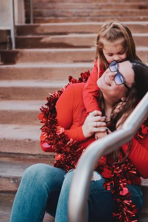 A couple sits on concrete steps with red tinsel garland sharing a tender moment in a romantic outdoor setting.