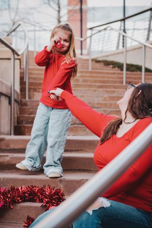 A candid moment on stairs with red holiday decorations as two people in matching red tops interact playfully.